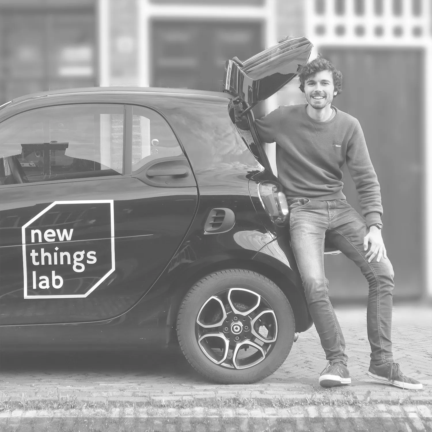 Nyckle leaning on a car with the New Things Lab logo